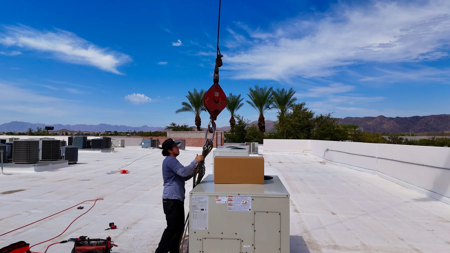 Technician preparing crane slings beside a commercial rooftop HVAC unit